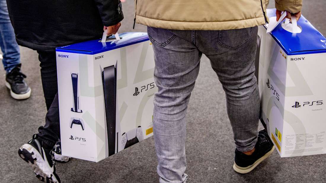 Two people carry a PlayStation 5 console. 